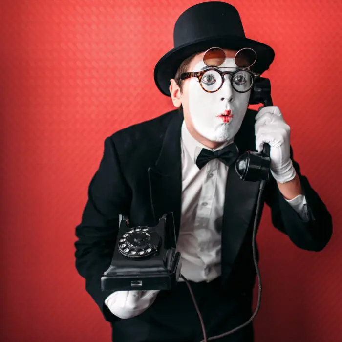 Mime theater actor performing with old telephone. Comedy pantomime artist in suit, gloves and hat